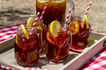 42149150-pitcher-y-tarro-de-albañil-tazas-llenas-de-té-y-limones-helado-sentado-en-la-mesa-de-picnic-con-mantel-co